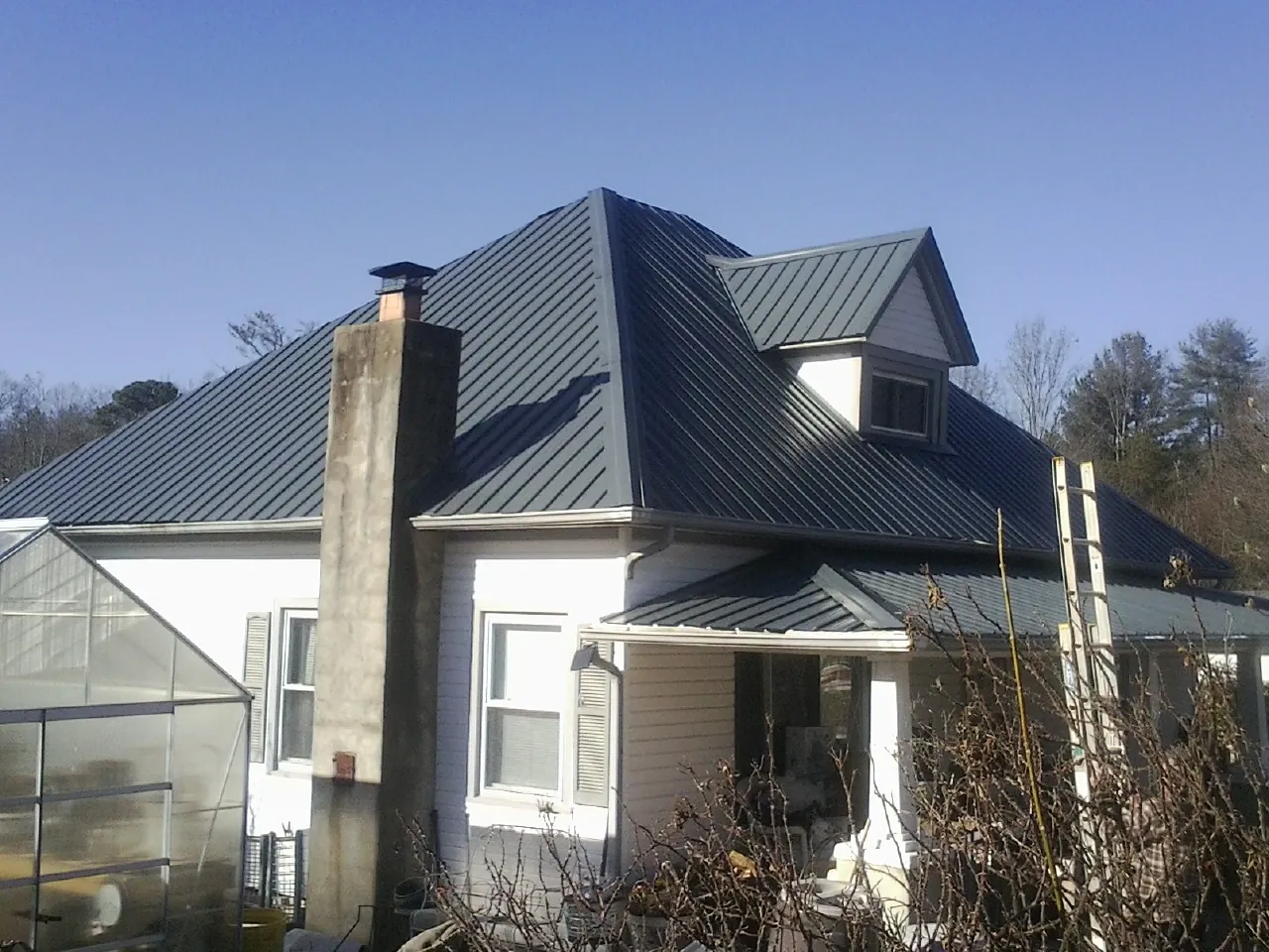 Dark blue standing seam metal roof on a white farmhouse with dormer — Slate & Tile Roof Repair by Roofing Brothers in Jefferson