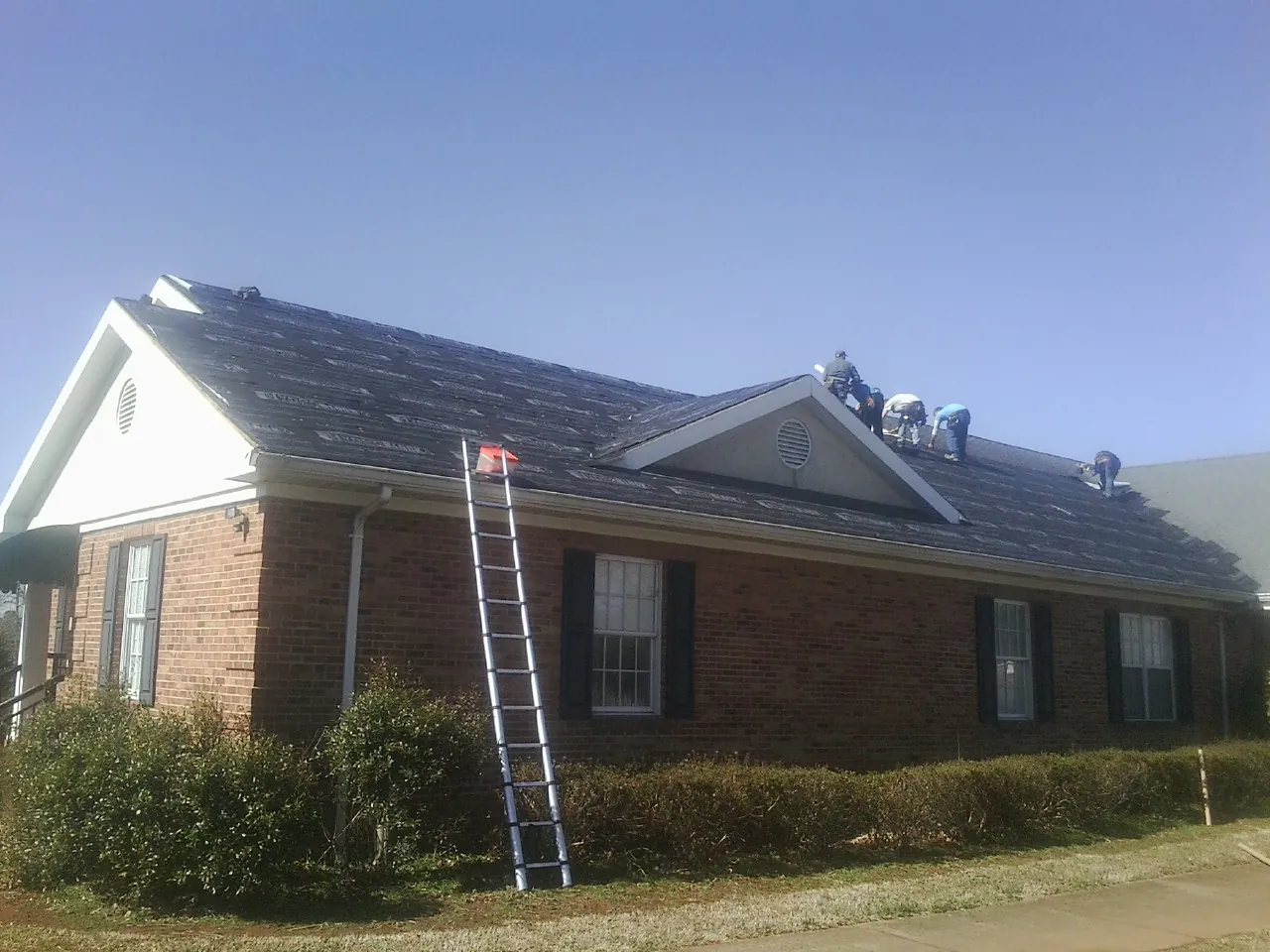 Crew tearing shingles off a brick ranch roof with a ladder set — Metal Roof Repair work by our crew in Jefferson