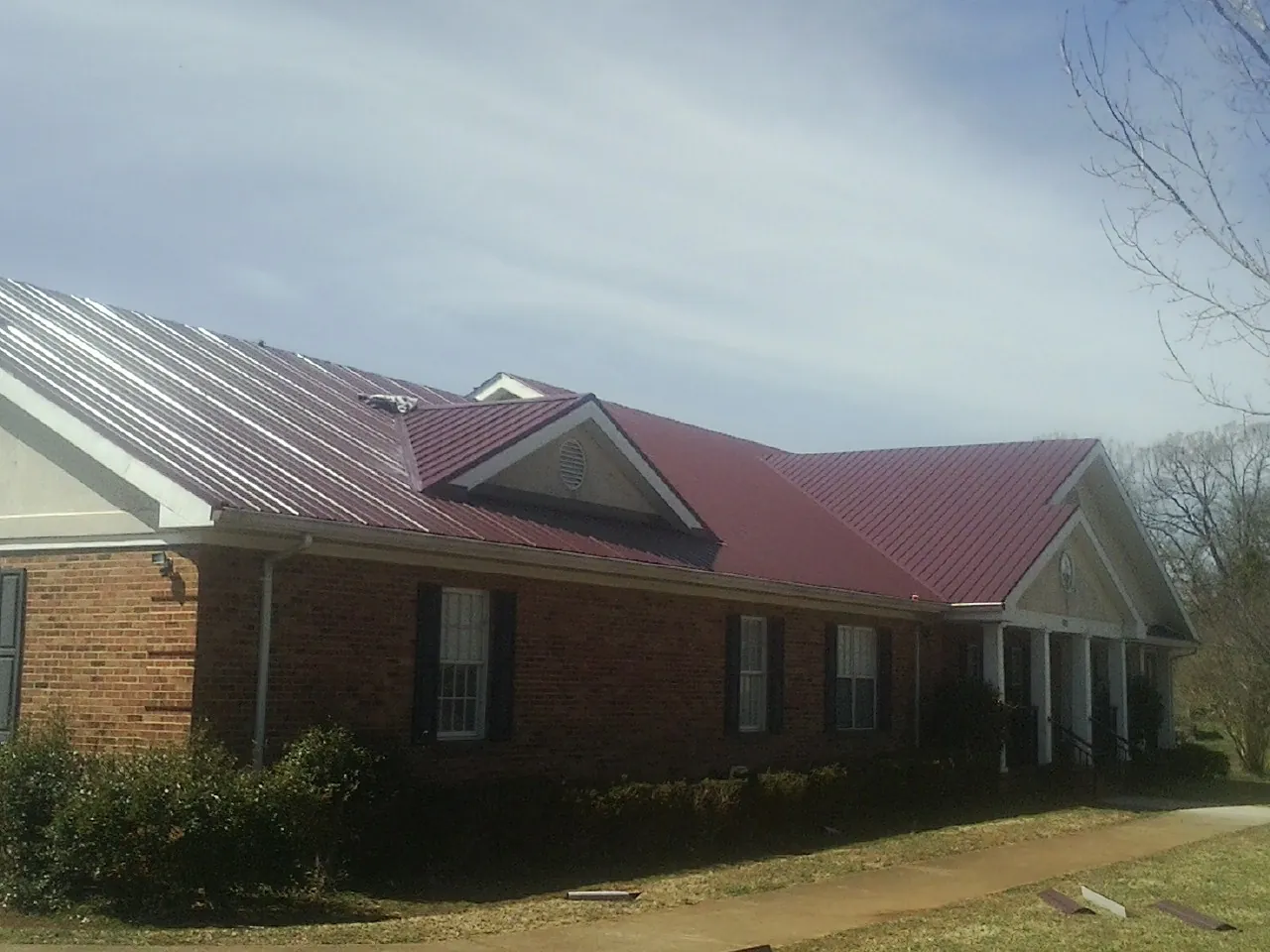 Red metal roof with gabled entries on a long brick building, from a Hail Damage Roof Repair job in Jefferson